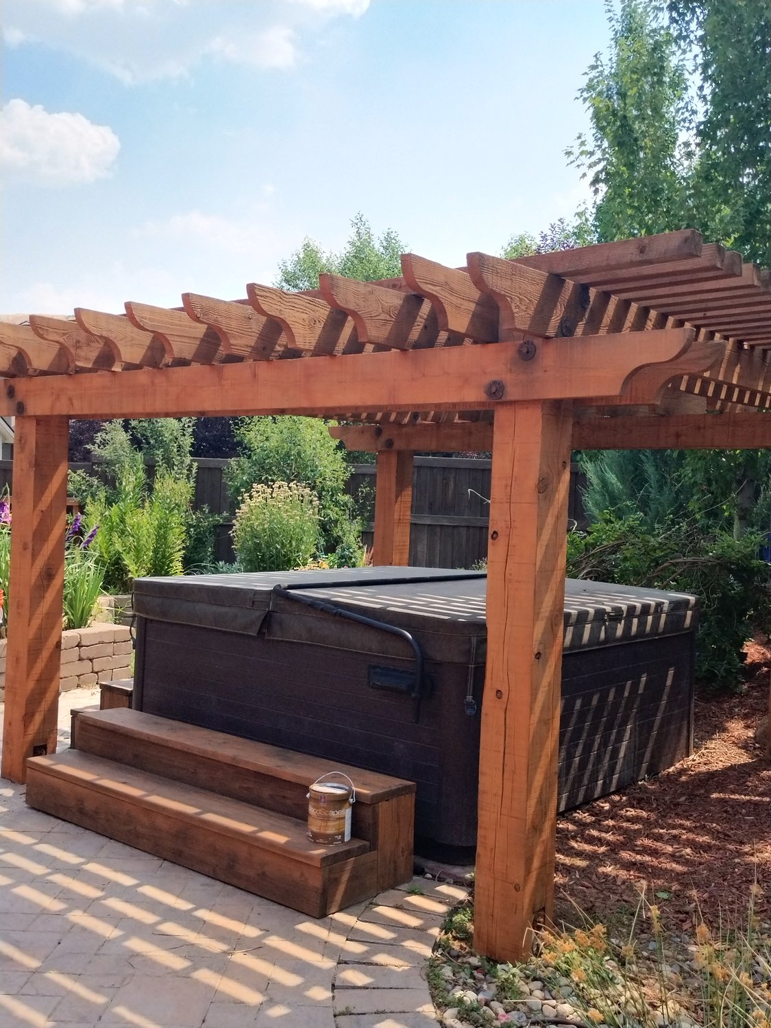 A stained wooden pergola in a sunny backyard with garden landscape