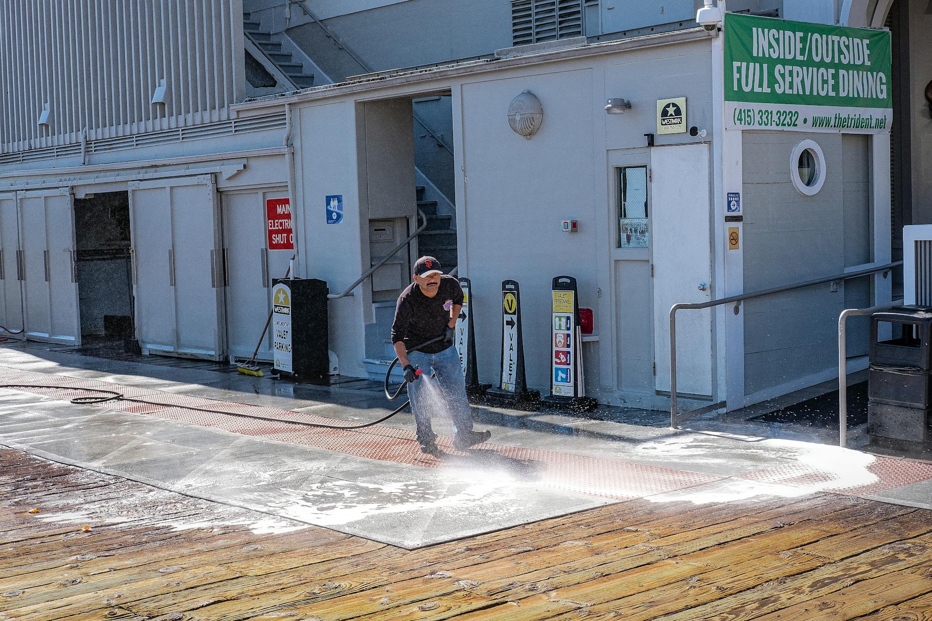 Worker pressure washing an outdoor wooden deck with high-pressure spray
